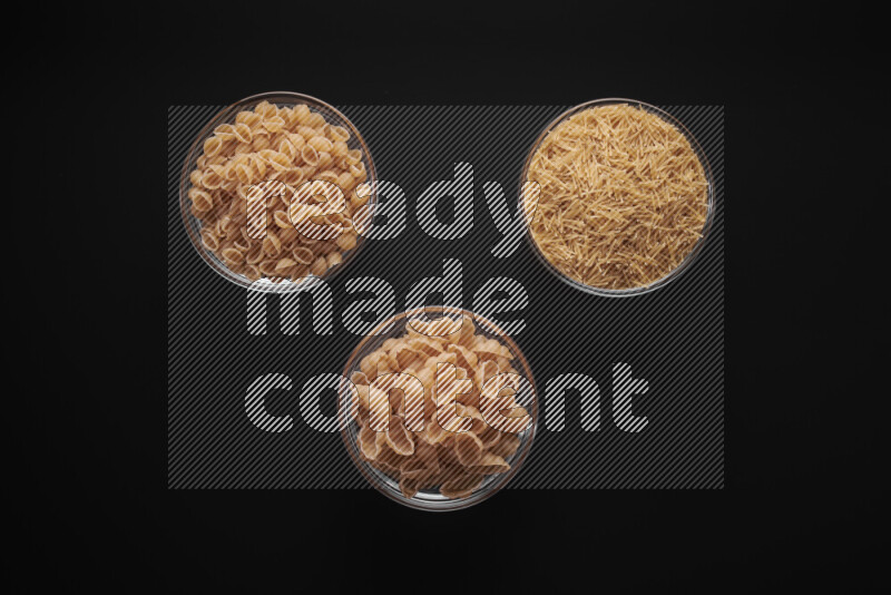 Different pasta types in glass bowls on black background
