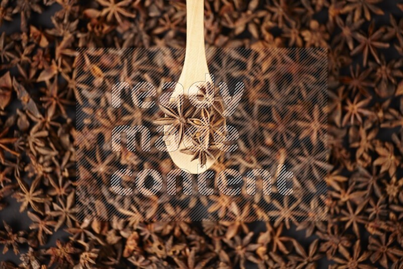 Star Anise in a wooden spoon on more stars anise filling the frame on black flooring