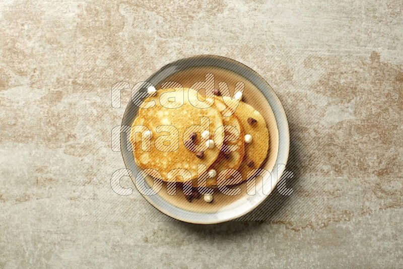 Three stacked chocolate chips pancakes in a bicolor plate on beige background