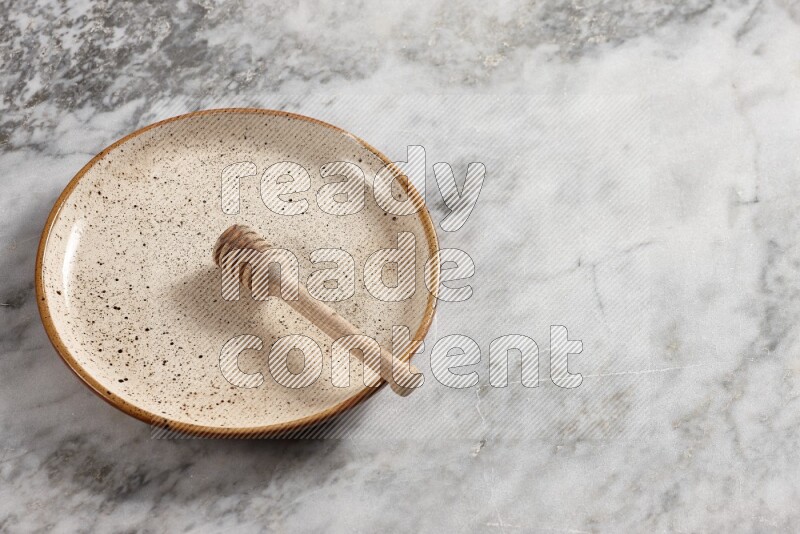 Beige pottery plate with wooden honey dipper in it on grey marble background