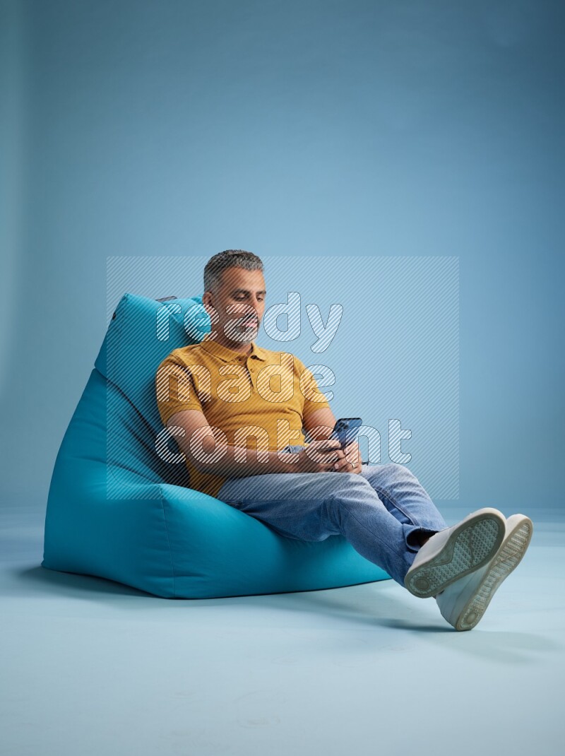 A man sitting on a blue beanbag and texting on phone