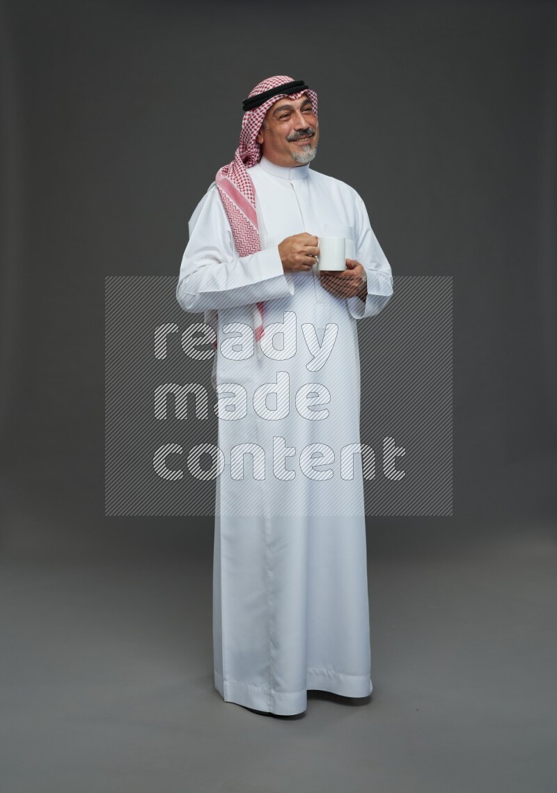 Saudi man with shomag Standing holding mug on gray background
