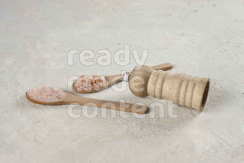 2 wooden spoons filled with fine and coarse salt with wooden grinder beside them on white background