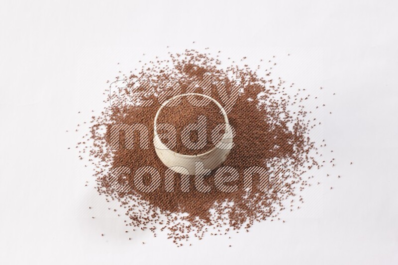 A beige pottery bowl full of garden cress seeds with more seeds spread on a white flooring