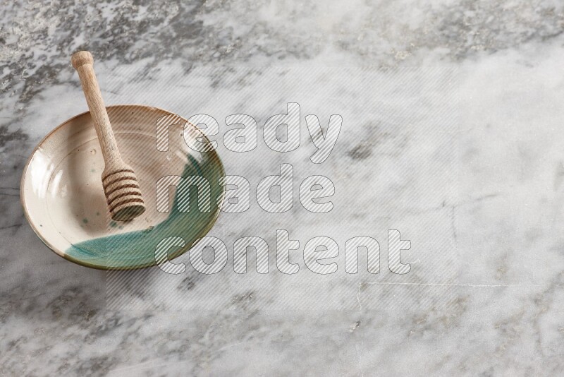Multicolored pottery plate with wooden honey dipper in it on grey marble background