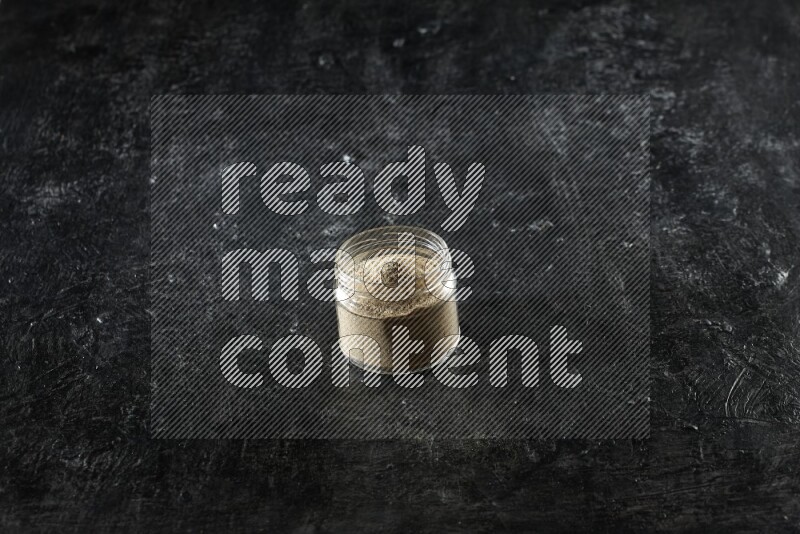 وعاء زجاجي ممتلئ ببودرة الهيل على خلفية سوداء