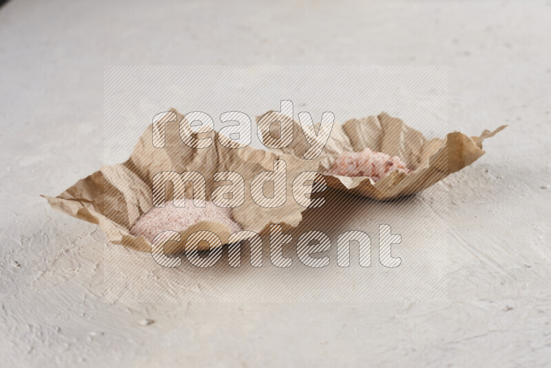 A crumpled piece of paper full of pink himalayan salt on white background