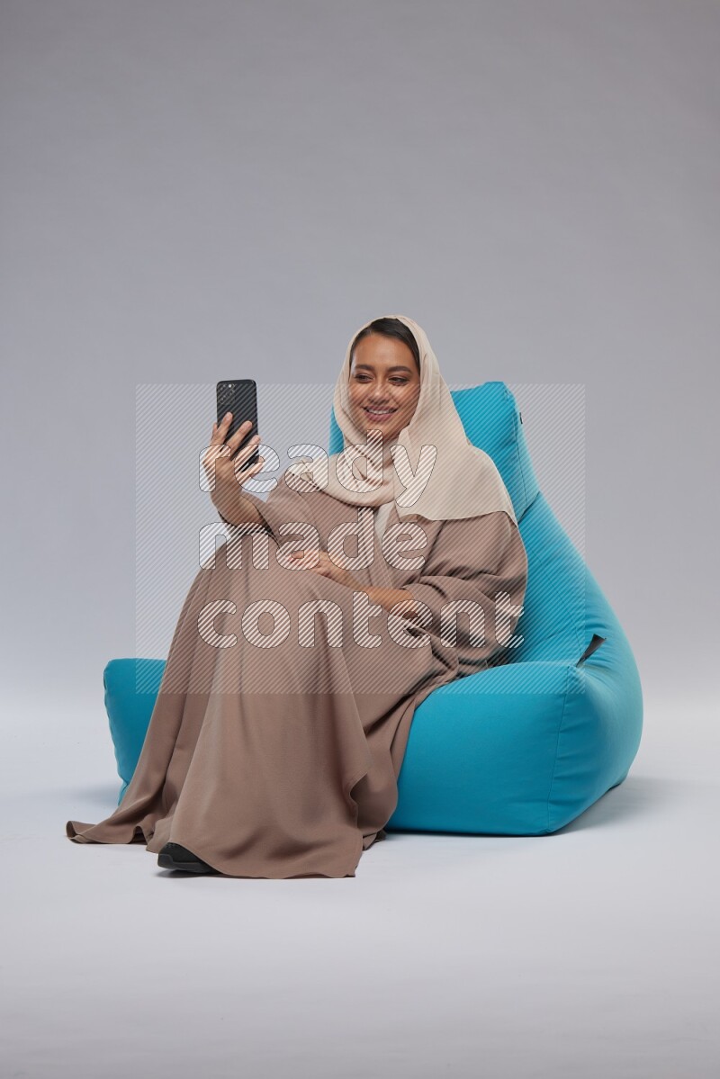A Saudi woman sitting on a blue beanbag and taking selfie
