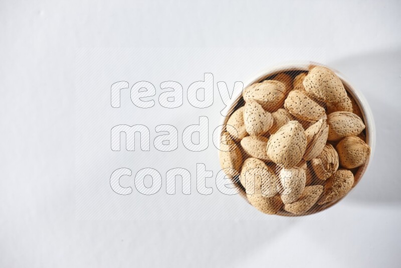 A beige ceramic bowl full of almonds on a white background in different angles