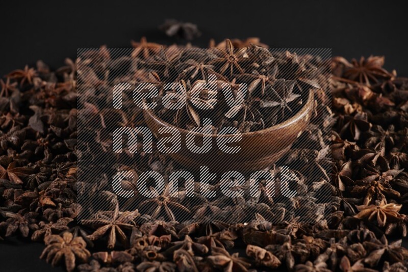 Star Anise in a wooden bowl and surrounded by more anise filling the frame on black flooring
