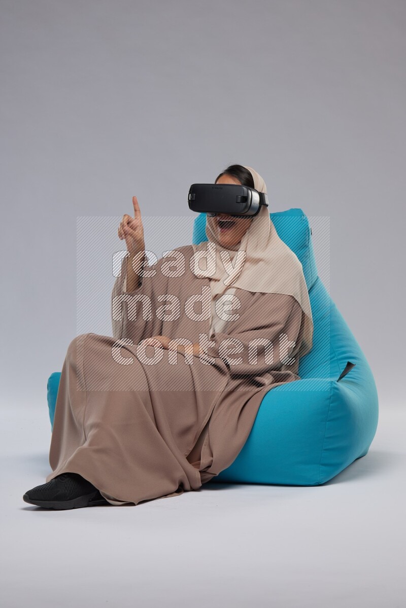 A Saudi woman sitting on a blue beanbag and gaming with VR