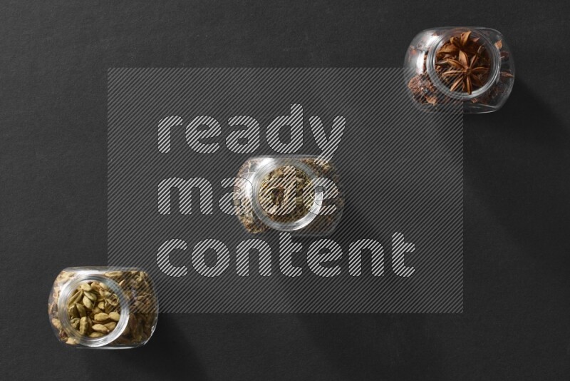 يانسون نجمي وريحان مجفف وحبوب الهيل في أوعية زجاجية علي خلفية سوداء