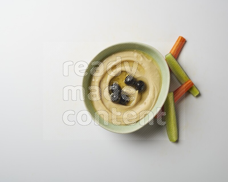 Hummus in a green plate garnished with black olives on a white background