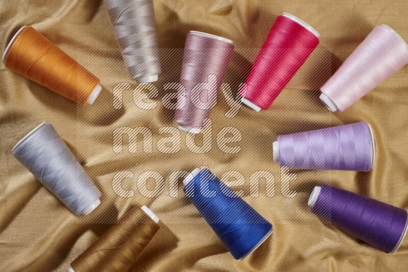 Multicolored sewing thread spools on yellow fabric background