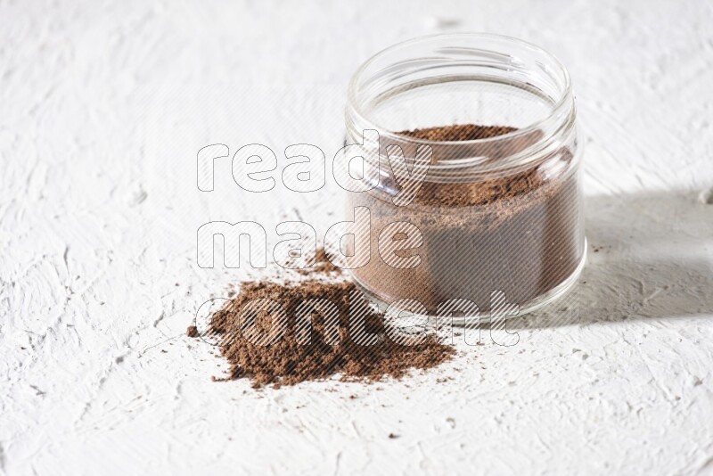 A glass jar full of cloves powder on a textured white flooring