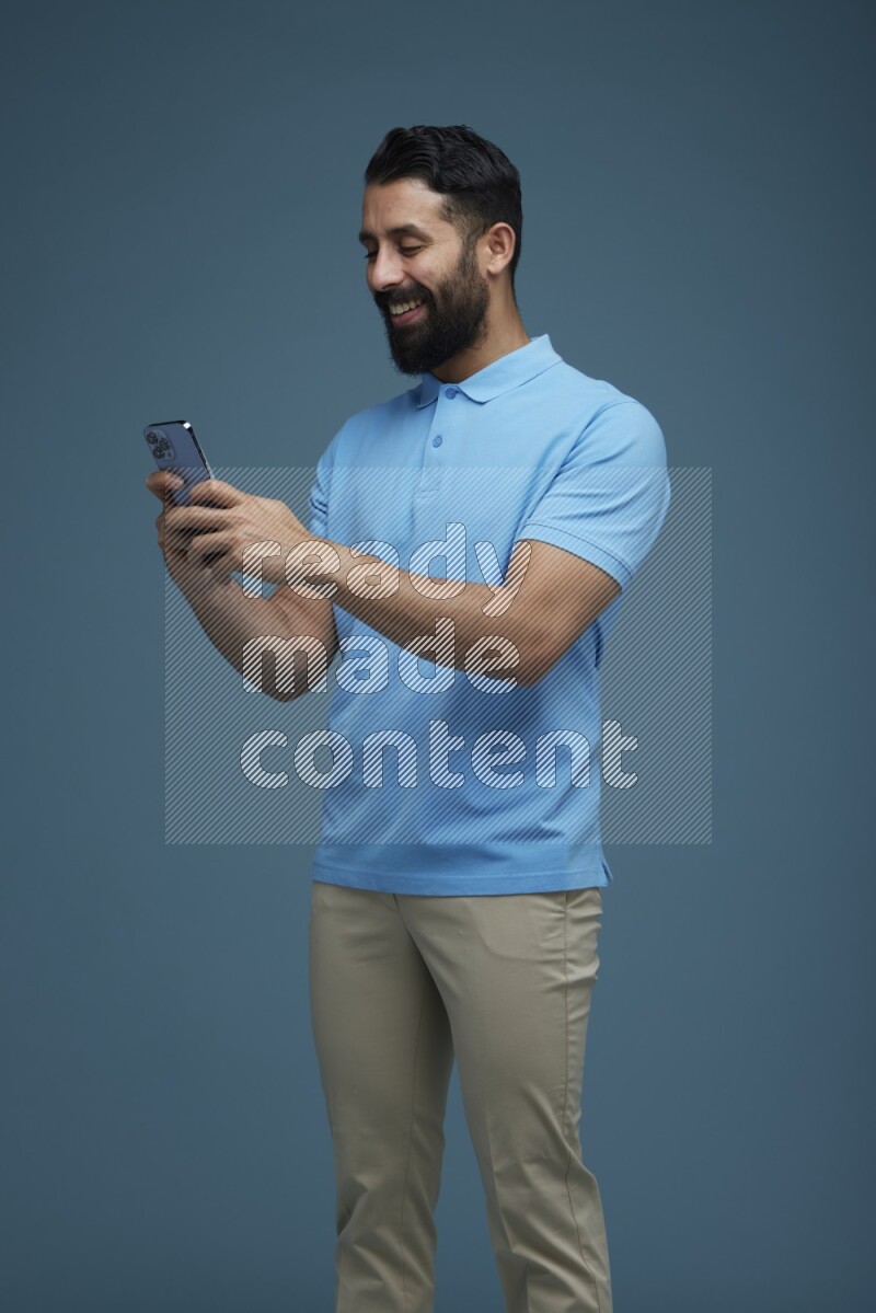 A man Texting on his phone in a blue background wearing a Blue shirt