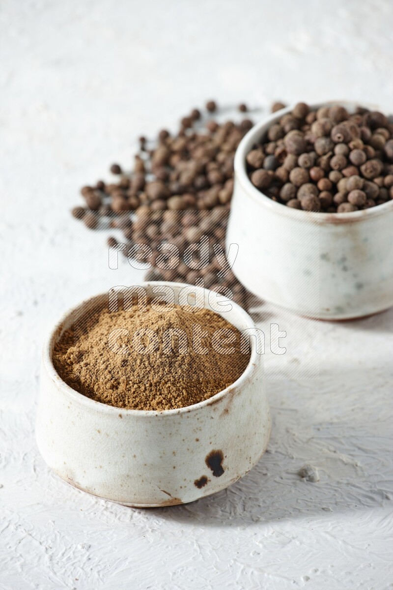 وعاءان بيج، أحدهما ممتلئ ببودرة بهار الفلفل الحلو والآخر بالحبوب مع البودرة والحبوب متناثرة على خلفية بيضاء