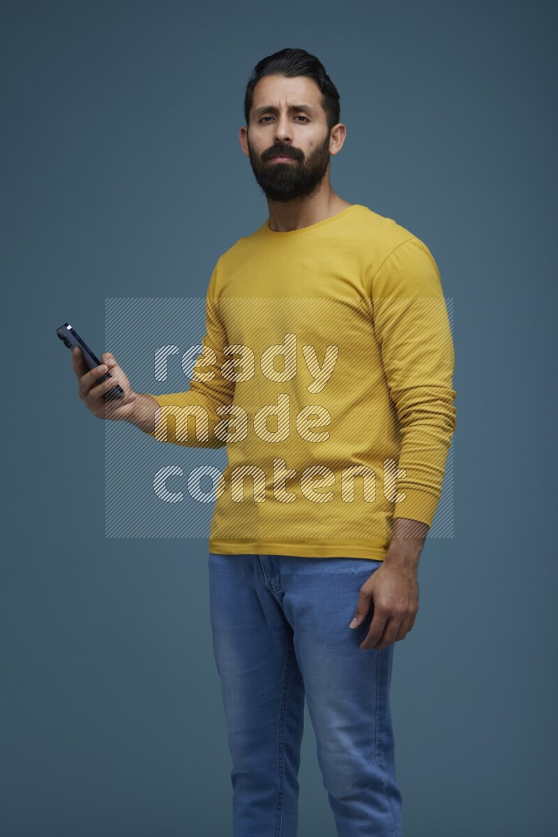 Man posing with a phone in a blue background wearing a yellow shirt
