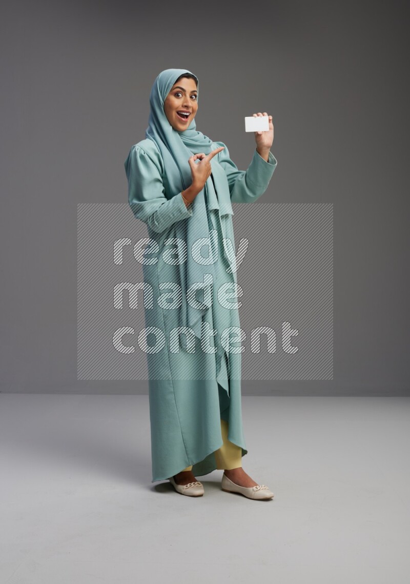 Saudi Woman wearing Abaya standing holding ATM card on Gray background