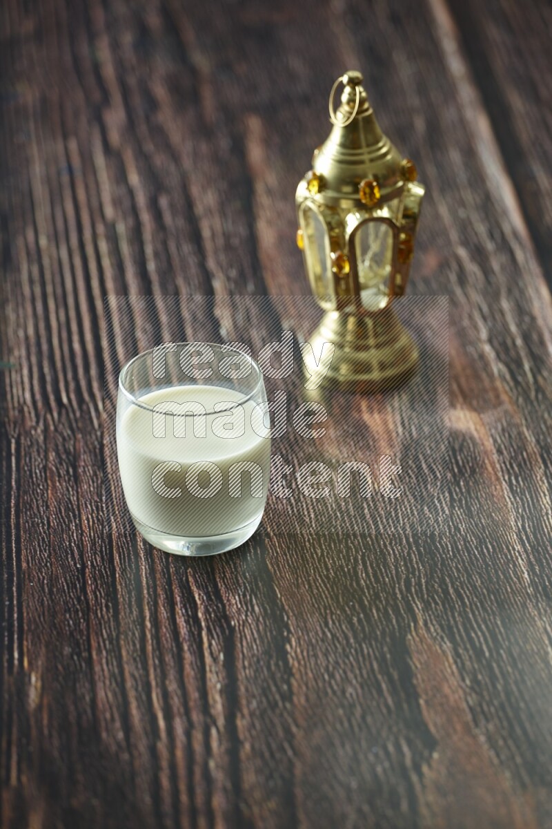 فانوس ذهبي مع مشروبات مختلفة وتمر ومكسرات وسبحة صلاة وقرآن على خلفية خشبية بنية