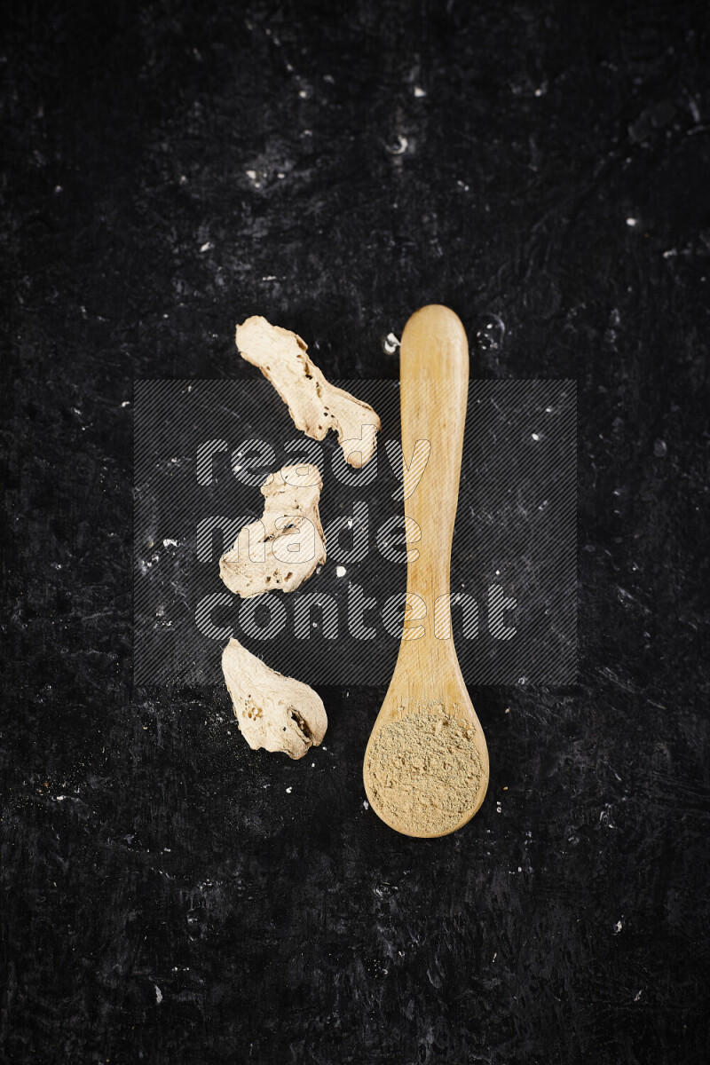 A wooden spoon full of ground ginger powder on black background