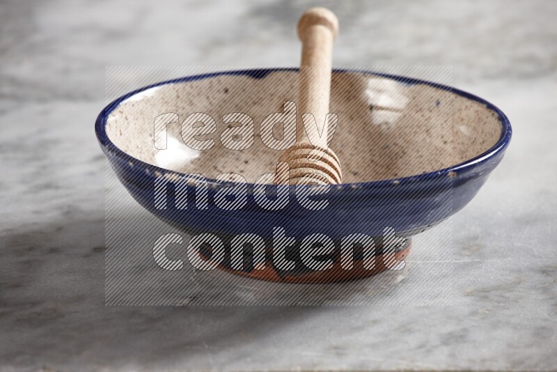 Multicolored pottery bowl with wooden honey dipper in it on grey marble background