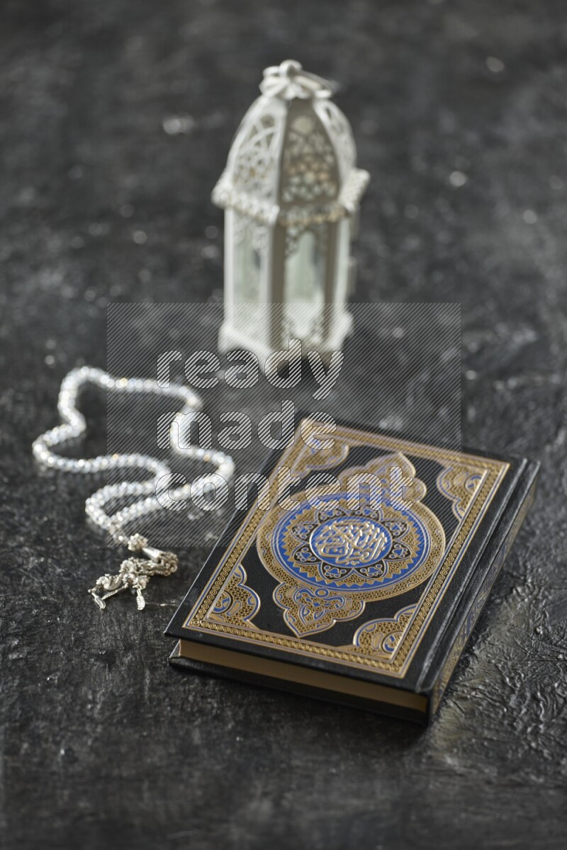 A white lantern with different drinks, dates, nuts, prayer beads and quran on textured black background
