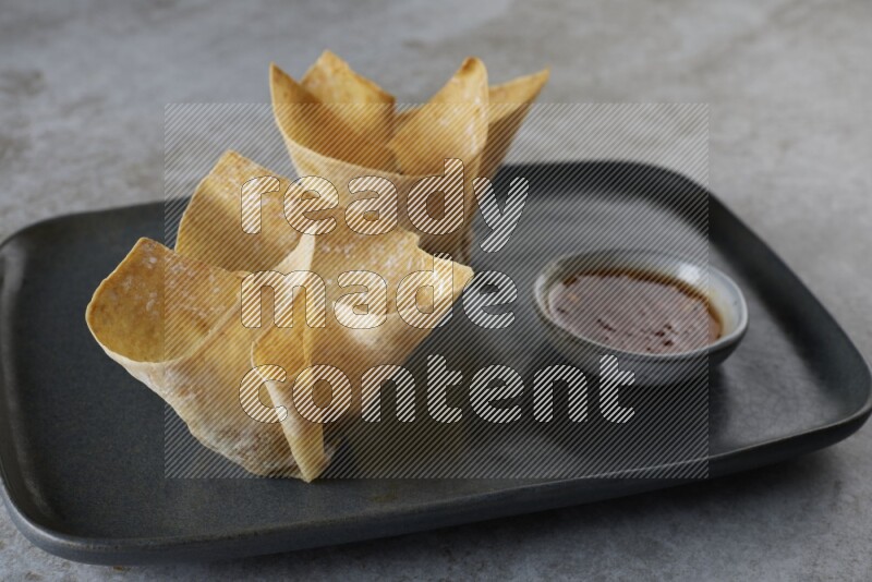 wonton cups with soy sauce ramkin on rectangle dark grey ceramic plate on grey textured counter top