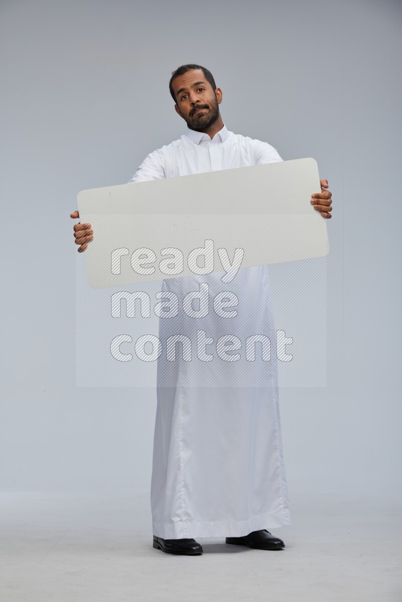 Saudi man wearing Thob standing holding board on Gray background