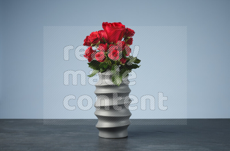 An arrangement of vivid red roses in a grey spiral vase on black marble background