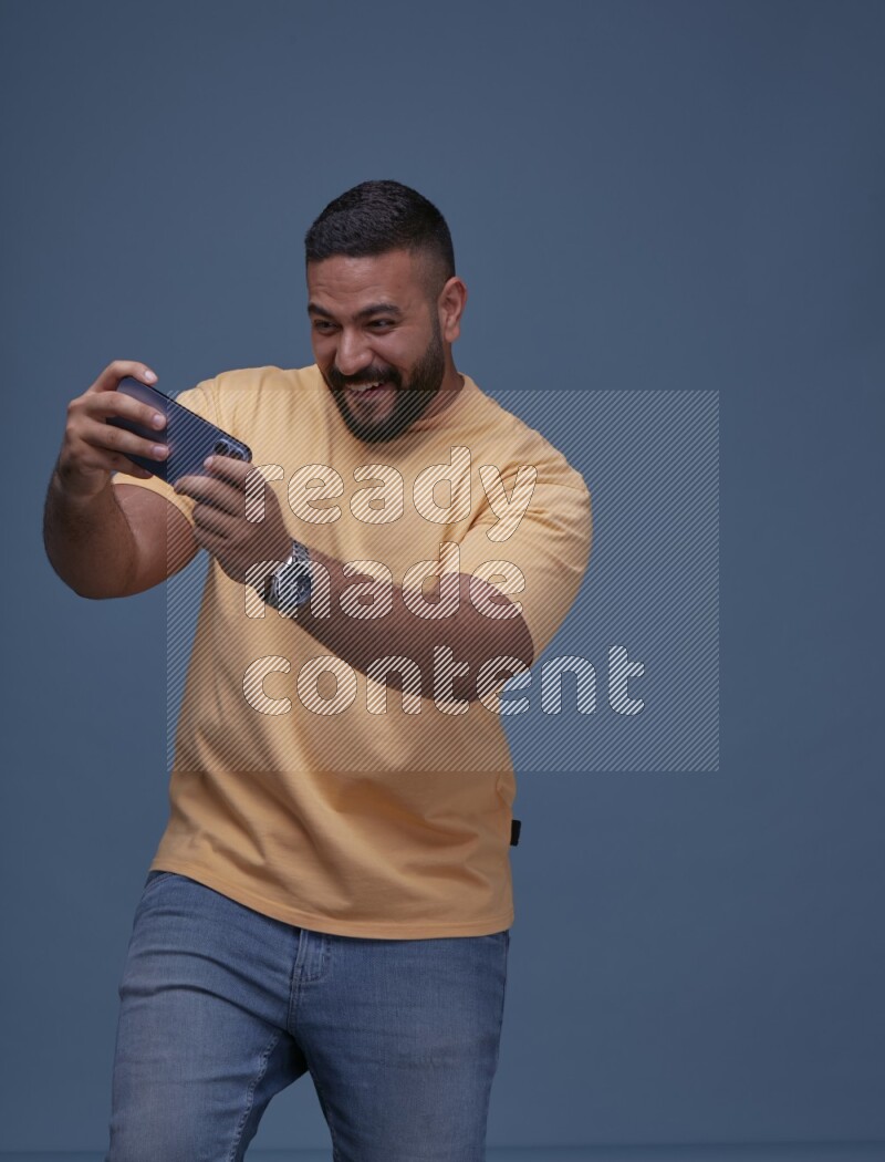 A man Playing Games on Smartphone on Blue Background wearing Orange T-shirt