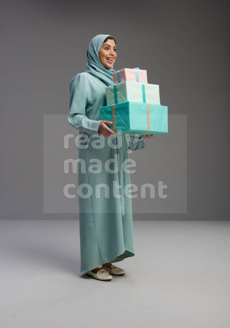 Saudi Woman wearing Abaya standing holding gift box on Gray background