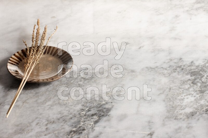 Wheat stalks on multicolored pottery plate on grey marble background