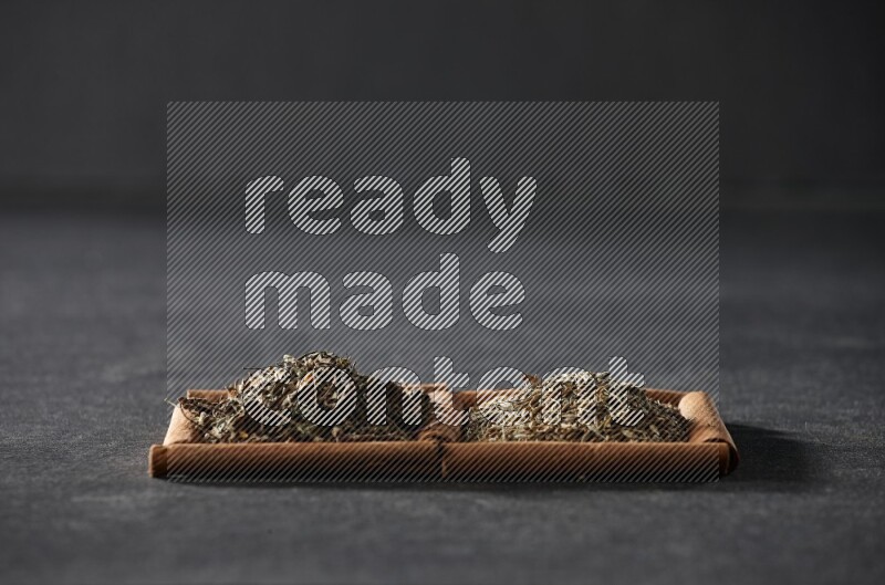 2 squares of cinnamon sticks full of cumin and dried basil on black flooring