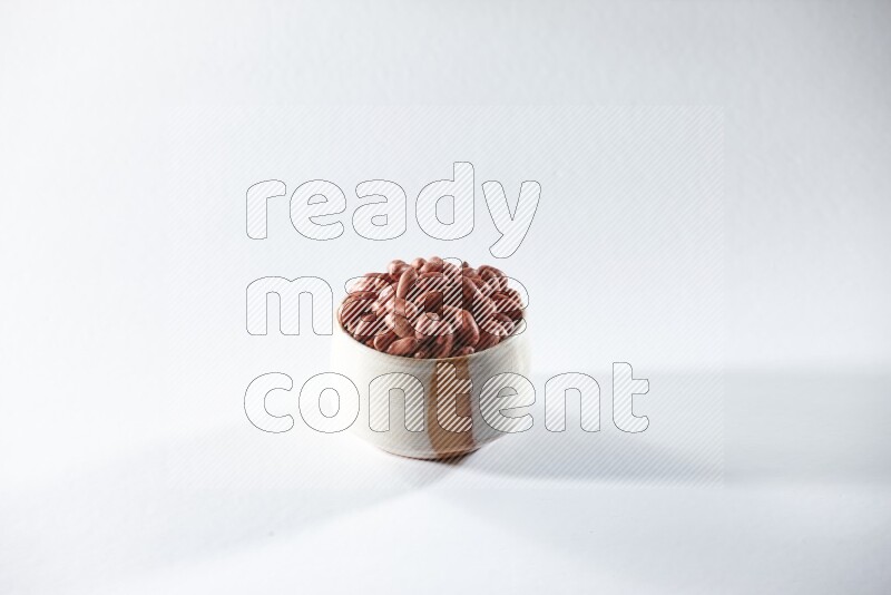 A beige ceramic bowl full of red skin peanuts on a white background in different angles