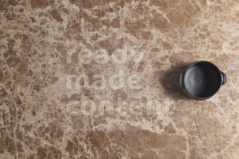 A black pottery bowl on beige marble background