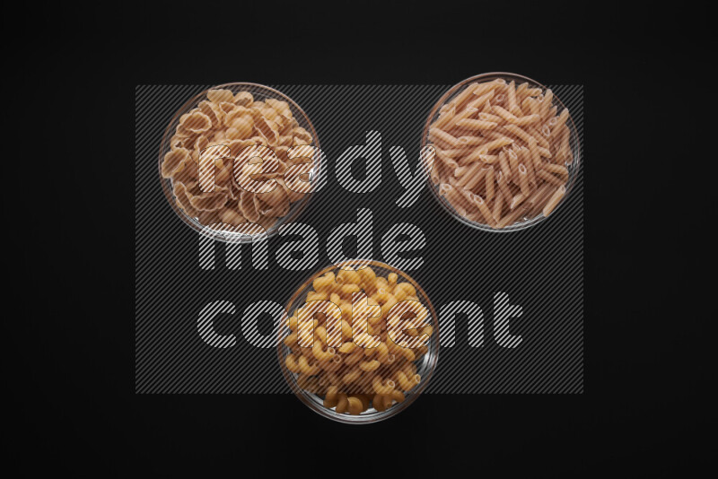 Different pasta types in glass bowls on black background