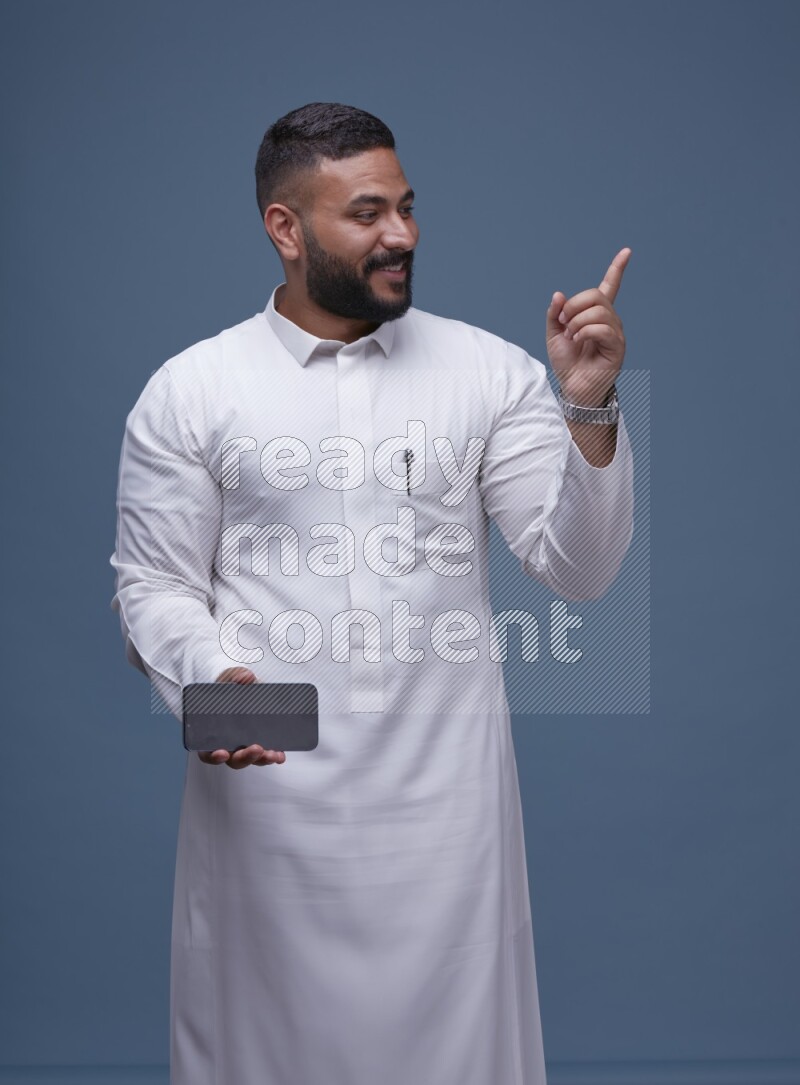 A man Showing his phone in Blue Background wearing Saudi Thob