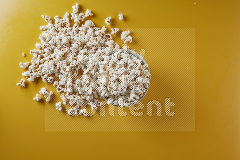 A white pottery bowl full of popcorn with popcorn beside it on a yellow background in different angles