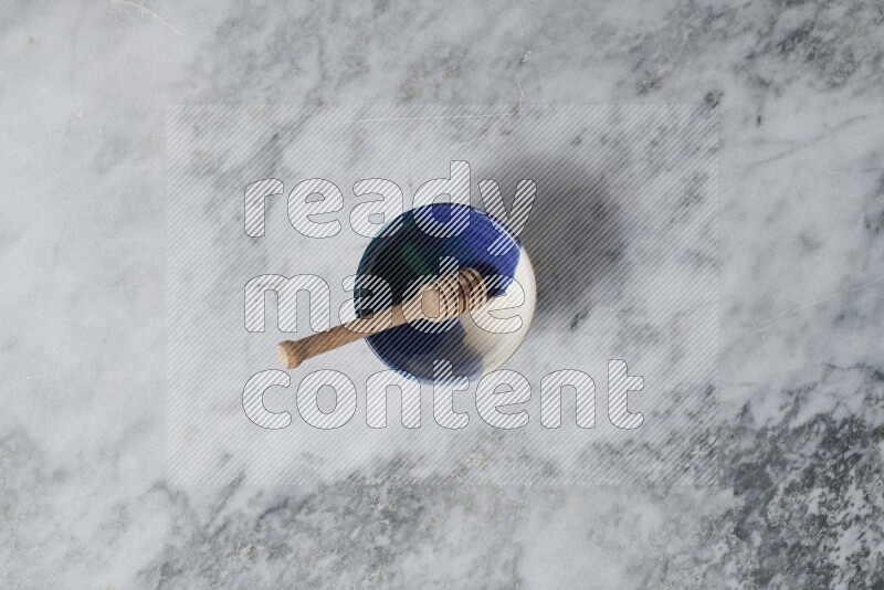 Multicolored pottery bowl with wooden honey dipper in it on grey marble background