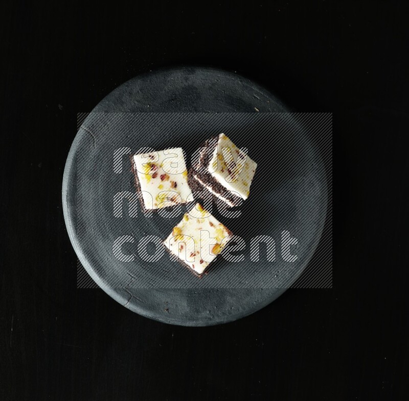 Assorted desserts in a black pottery plate on black background