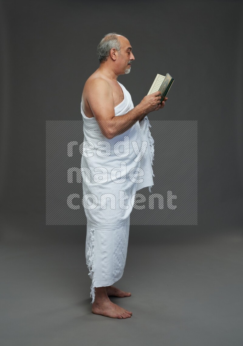 A man wearing Ehram Standing reading quran on gray background