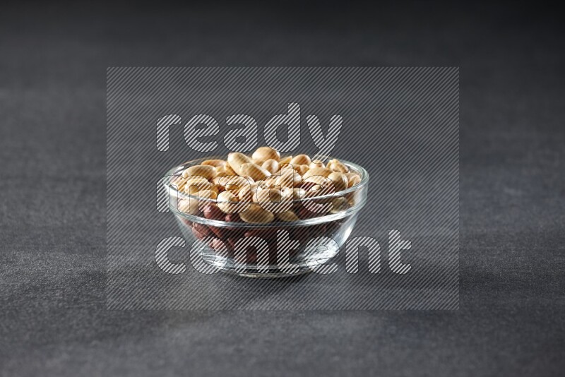 A glass bowl full of peeled peanuts on a black background in different angles