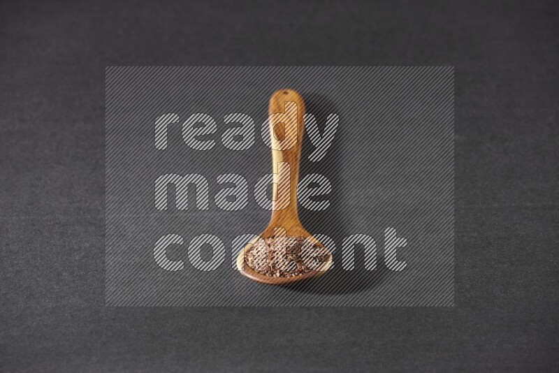 A wooden ladle full of flaxseeds on a black flooring