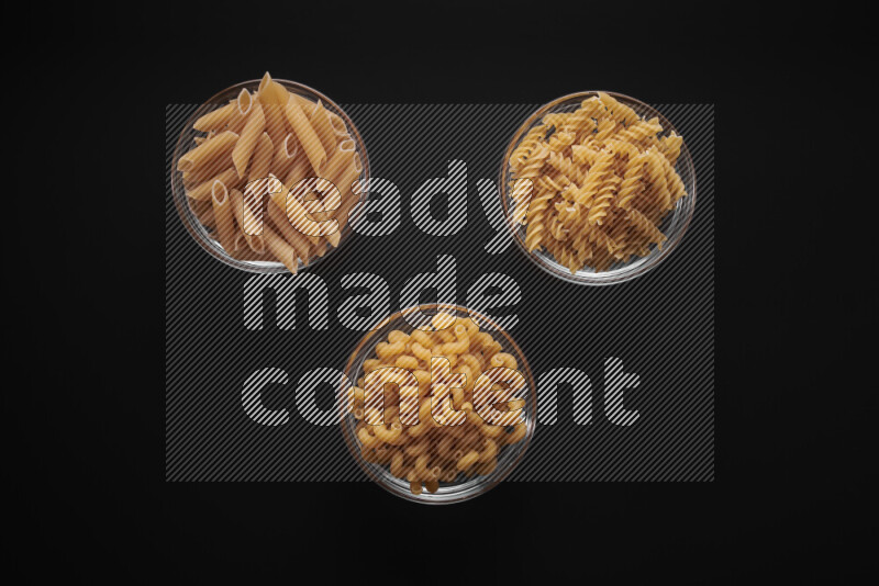 Different pasta types in glass bowls on black background