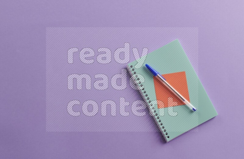 A blue notebook with school supplies on purple background