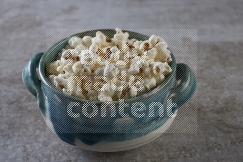 popcorn in a multi-colored handheld ceramic bowl on a grey textured countertop