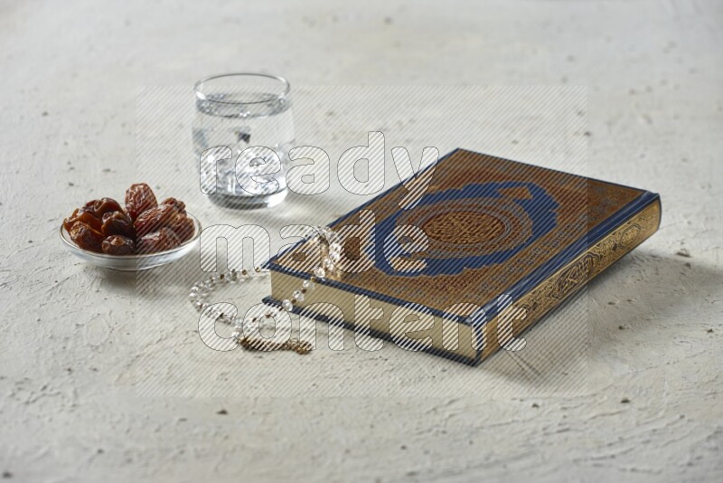 Quran with dates, prayer beads and different drinks all placed on textured white background