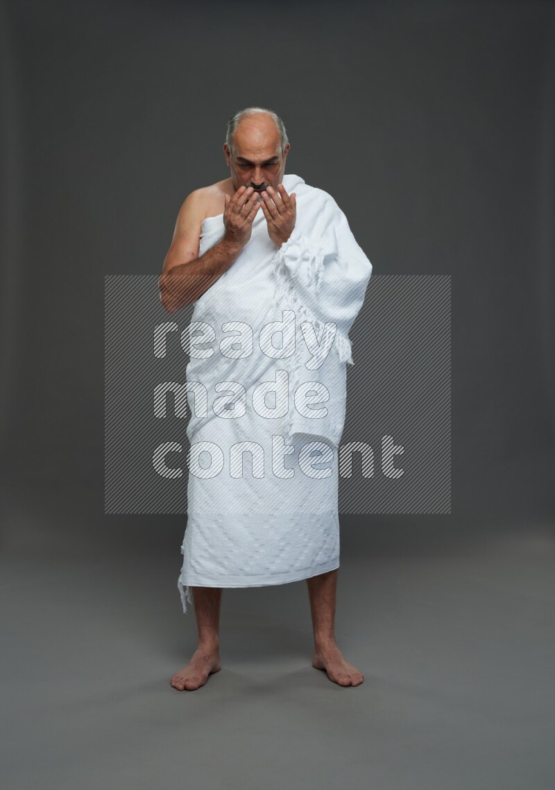 A man wearing Ehram Standing dua'a on gray background