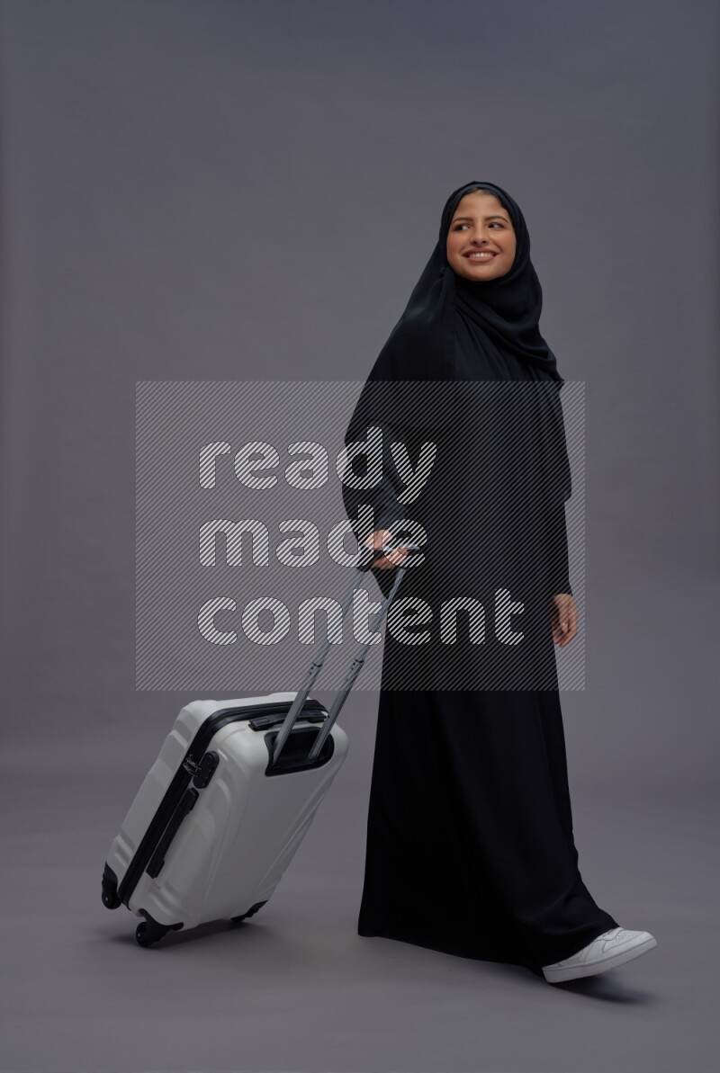 Saudi woman wearing Abaya standing holding bag on gray background